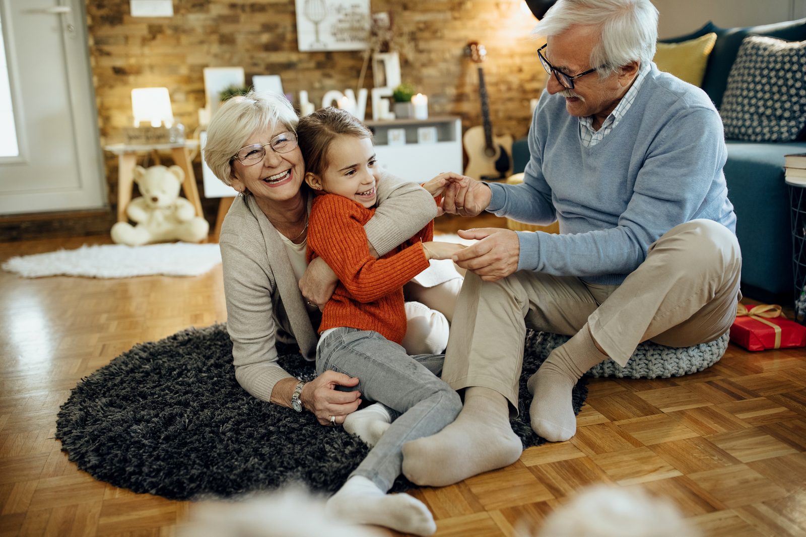 A grandfather and grandmother laughing with their granddaughter at home
